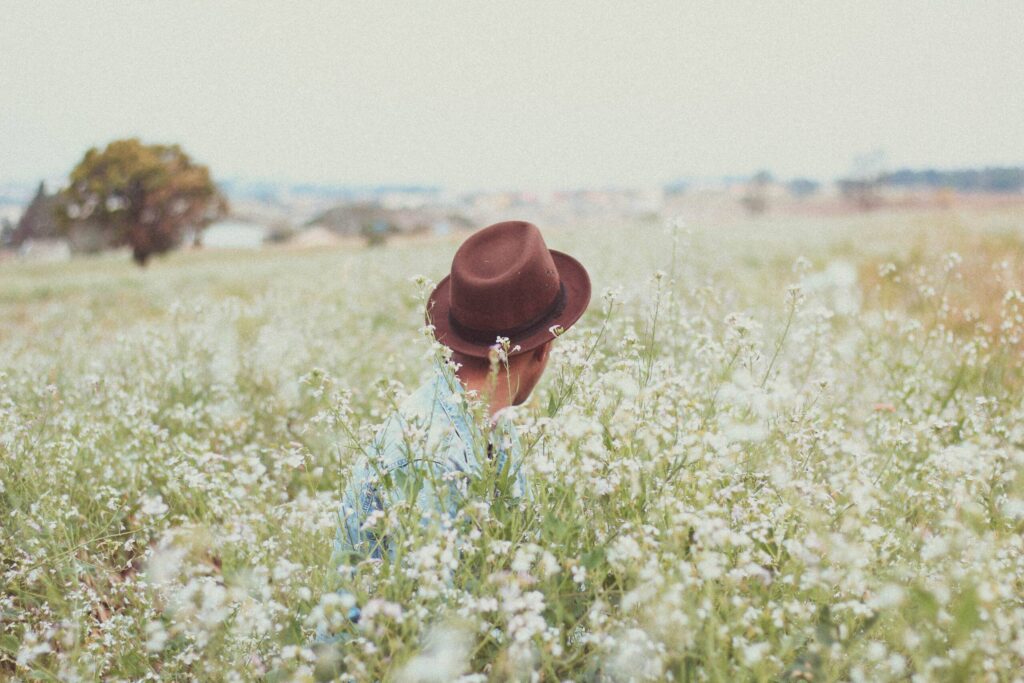 Man with hat in field of wildflowers.