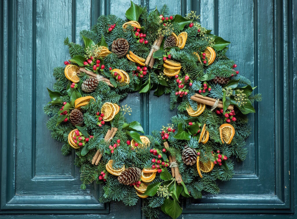 Festive wreath with greenery and decorations including cinnamon, dried oranges and pine cones.