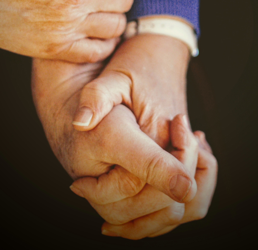 Two elderly hands clasped tightly together.